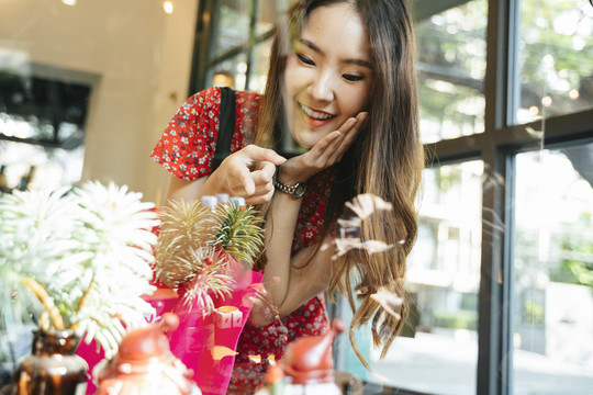 一位身穿红色连衣裙的年轻亚洲妇女兴奋地看着玻璃墙后面的东西。逛街。