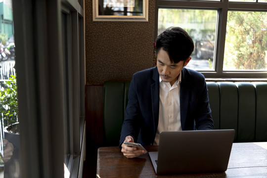穿着正装的亚泰商人坐在咖啡馆里用智能手机和笔记本电脑，在户外工作。