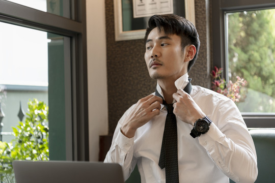 穿着白领衬衫的亚洲商人在笔记本电脑前打扮自己。工作和穿衣。