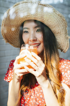 在甜点咖啡厅，一位身着红色连衣裙、头戴草帽、喝着冰镇果汁的快乐泰国亚裔年轻女子。