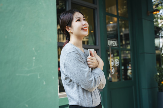 科技爱好者-美丽的亚洲年轻女子手持平板电脑，双手站在咖啡店外。
