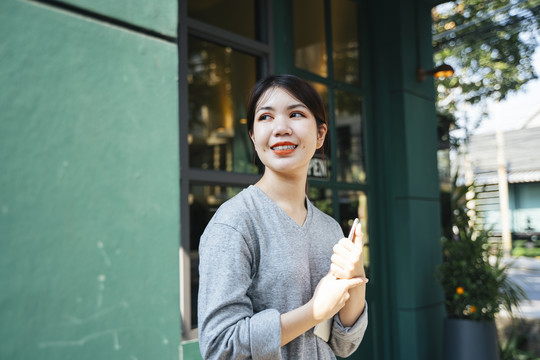 科技爱好者-美丽的亚洲年轻女子手持平板电脑，双手站在咖啡店外。