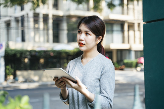 年轻漂亮的亚洲女人用平板电脑走在街上。现代。