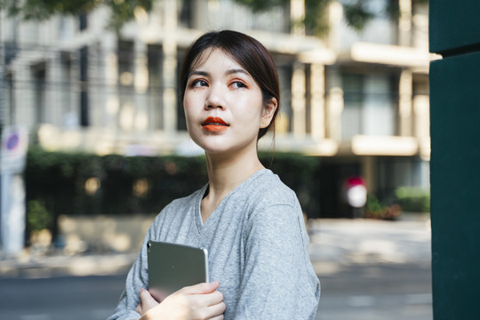 美丽的亚洲年轻女子手持平板电脑走在街上。