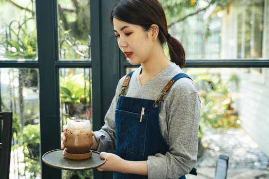 美丽的亚泰女服务员在咖啡厅为顾客提供冰镇咖啡。