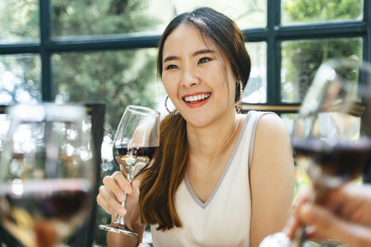 开朗快乐的亚洲女人穿着白色连衣裙，和朋友一起享受聚会，举着酒杯，和朋友聊天。