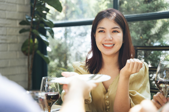 一个快乐的亚洲女人在餐馆里从朋友手里抓起盘子。