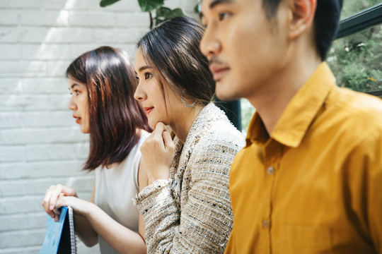 美丽的亚洲女人和其他候选人坐在房间外等待面试。忧心忡忡、紧张不安的应聘者前来面试，等待答案。带着简历