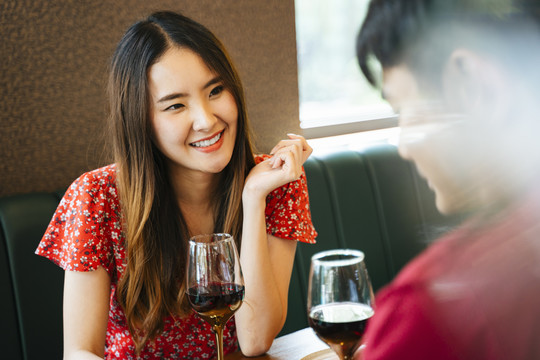 在情人节庆祝。一位穿着红裙子的美丽快乐的亚洲女人在餐馆酒吧和她的男朋友约会。