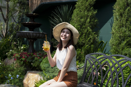 美丽的泰国亚裔女子在花园里享用热带西番莲果汁。