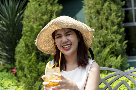 美丽的亚泰女子戴着帽子，在花园里畅饮百香果汁。