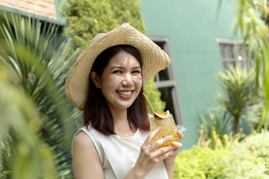 特写照片快乐的亚洲女人戴着帽子享受果汁。
