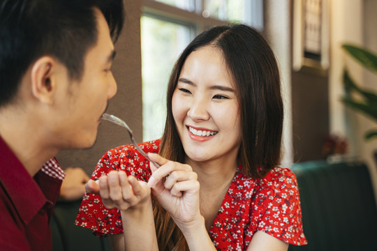 美丽的亚洲女人用叉子喂男友甜点蛋糕。