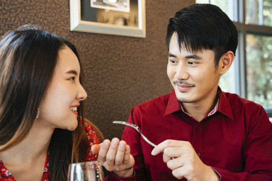 穿着红衫的泰国帅哥用叉子给他的女孩喂食物。浪漫时刻。情人节的概念。