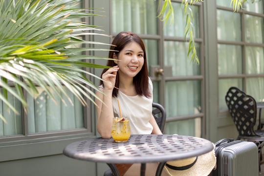 兴高采烈的亚洲女人坐在咖啡馆外喝着西番莲果汁。