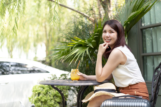 美丽开朗的亚泰女人坐在户外的椅子上，喝着热带西番莲果汁。