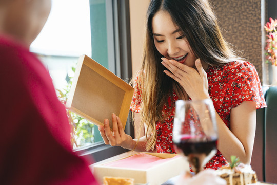 一位穿着红色连衣裙的亚洲女士打开了她从男朋友那里得到的礼物盒。