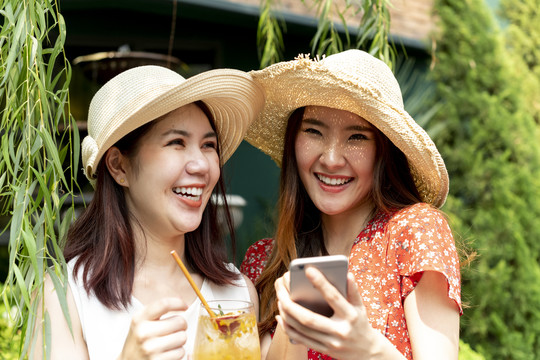 两个戴着帽子的亚泰游客一起在大自然中旅行。用智能手机拿着一杯果汁。