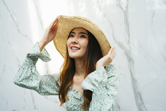 一个年轻漂亮的亚洲长发女人戴着帽子，穿着绿色的时尚衬衫站在花岗岩背景上的特写镜头。