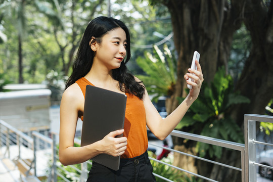 穿着橙色衬衫的亚洲美女用手机自拍。漂亮女人用智能手机视频通话。