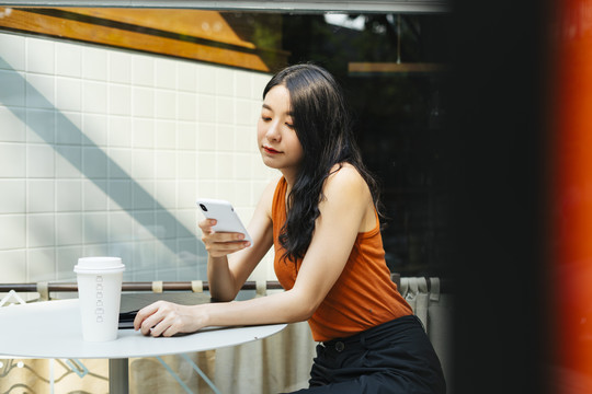 在咖啡厅，穿着橙色衬衫的亚洲美女用智能手机。