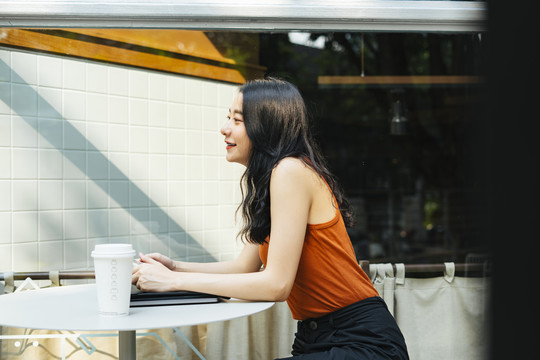侧视亚洲美女穿着橙色衬衫在咖啡厅放松。