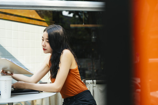 一位穿着橘色衬衫的亚洲美女在咖啡厅和别人聊天。