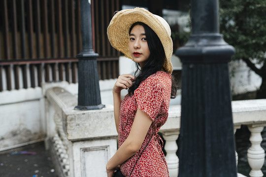 年轻漂亮的泰国亚裔旅行家妇女的侧视图，她穿着红色的裙子，戴着红色的帽子。
