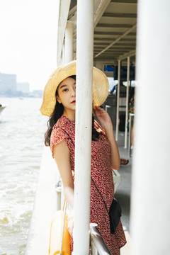 年轻漂亮的泰国亚裔旅行家，身穿红色连衣裙，头戴红帽，在湄南河乘船旅行。