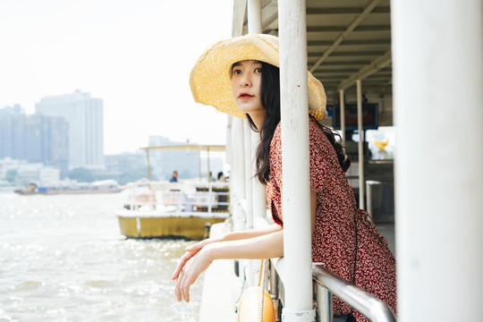 年轻漂亮的泰国亚裔旅行家，身穿红色连衣裙，头戴红帽，在湄南河乘船旅行。