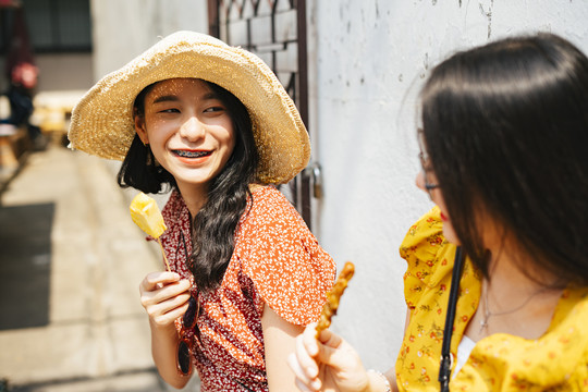 两位年轻漂亮的泰国亚裔旅行家女闺蜜一起在泰国享受街头美食。