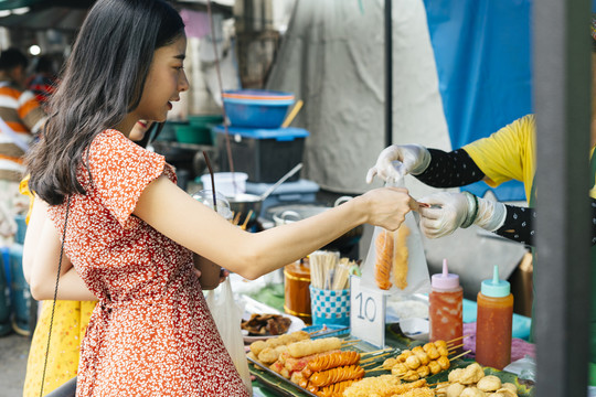 在泰国，一位亚洲妇女在街头买油炸热狗。