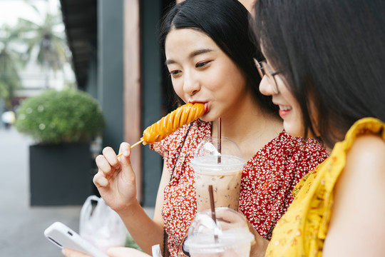 美丽的亚洲女人喜欢吃油炸热狗与朋友-街头美食的概念。