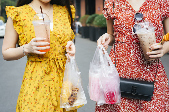 两个美丽的亚洲女人背着装满街头食物的塑料袋走在街上。