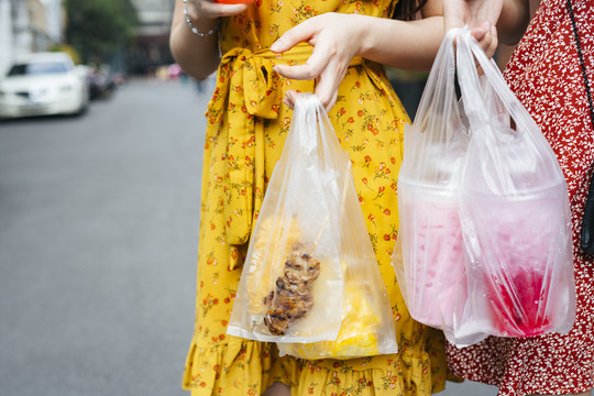 两个美丽的亚洲女人背着装满街头食物的塑料袋走在街上。