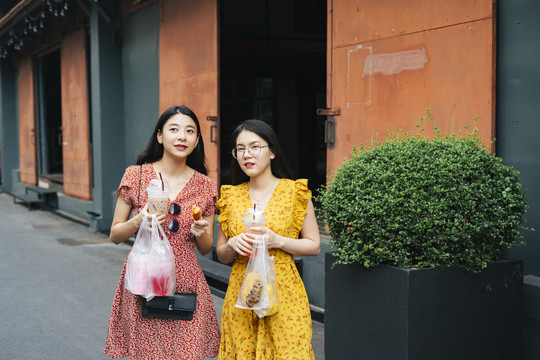 在泰国，两位美丽的亚洲年轻女子喜欢在街上吃美食，走在街上。