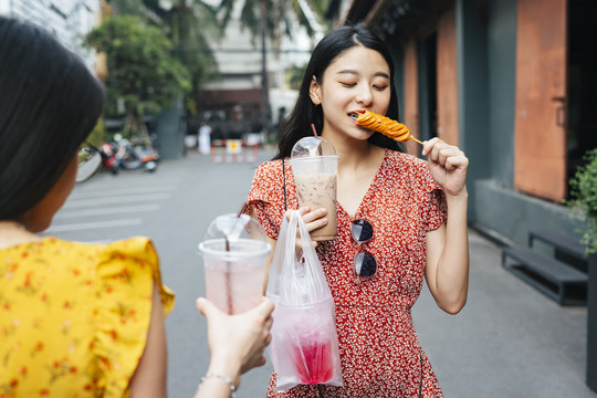 穿着红裙子的亚洲美女和穿着黄裙子的朋友一起吃街边小吃。