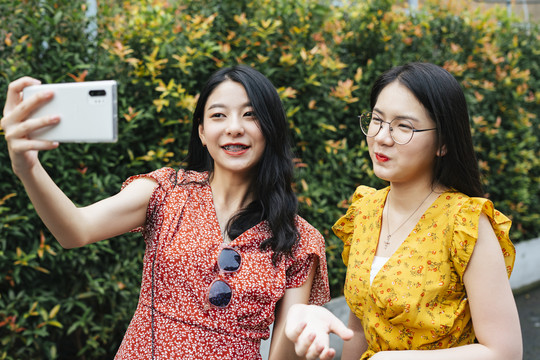 两位亚洲美女用智能手机自拍。录影或录像。在泰国旅游时，快乐美丽的女游客。