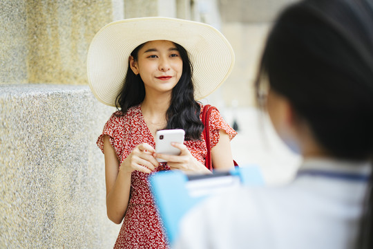 美丽的亚洲女游客穿着红色的裙子，戴着红色的帽子，在城市里和导游交谈。