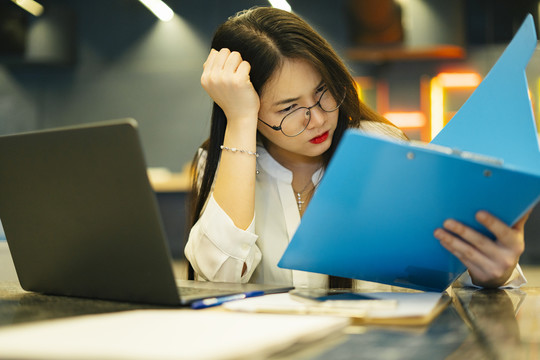 满是压力的年轻女商人在办公室里忙着做文书工作。坐在笔记本电脑前面的工作台上。