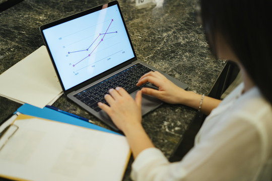 在办公室里，一个正在笔记本电脑上工作的女商人正在看屏幕上的收入线图。