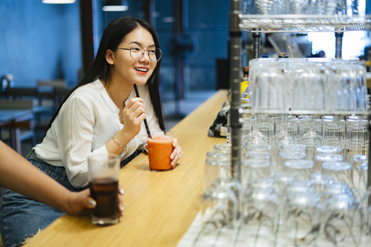 戴眼镜的亚洲美女在酒吧喝健康果汁。