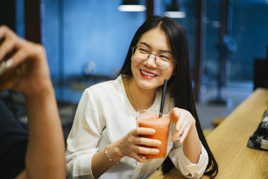 美丽的亚洲女人戴着眼镜坐在酒吧下班后，喝果汁。