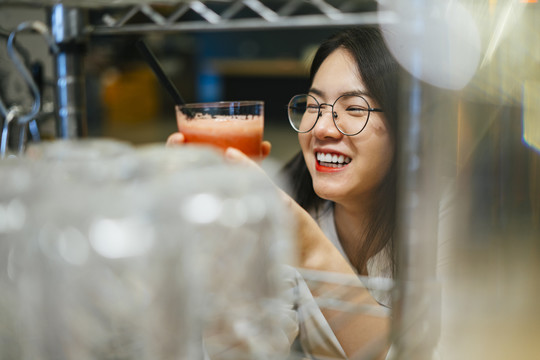 戴眼镜的亚洲美女喜欢在吧台后面喝健康果汁。