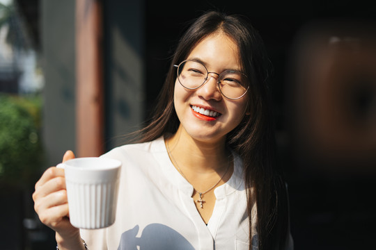 快乐的亚洲女人戴着眼镜拿着一杯咖啡。早上喝咖啡。