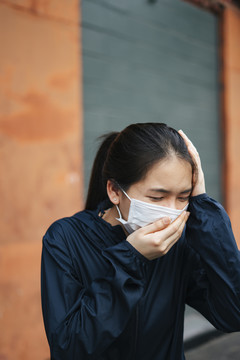 一名戴口罩的亚洲妇女因城市烟雾而咳嗽。双手捂着头。不健康的状况。