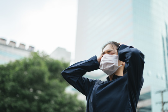 戴着口罩的亚洲妇女在烟雾中暴露太久后头痛。