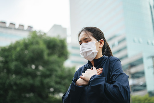 戴着口罩的亚洲妇女在城市里行走时不能呼吸。