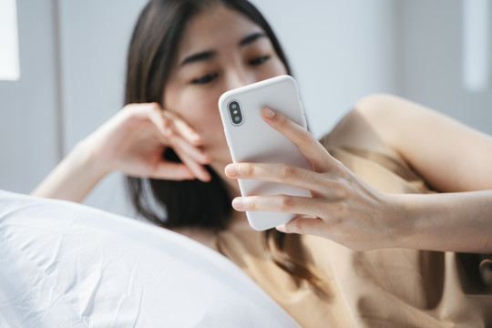 女孩弯腰躺在枕头上，打开她的社交媒体账户时，手中的智能手机截图。