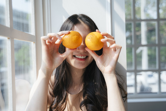 早上，一个卷曲的长发女孩站在窗前，手里拿着橘子，眼睛里举着橘子。